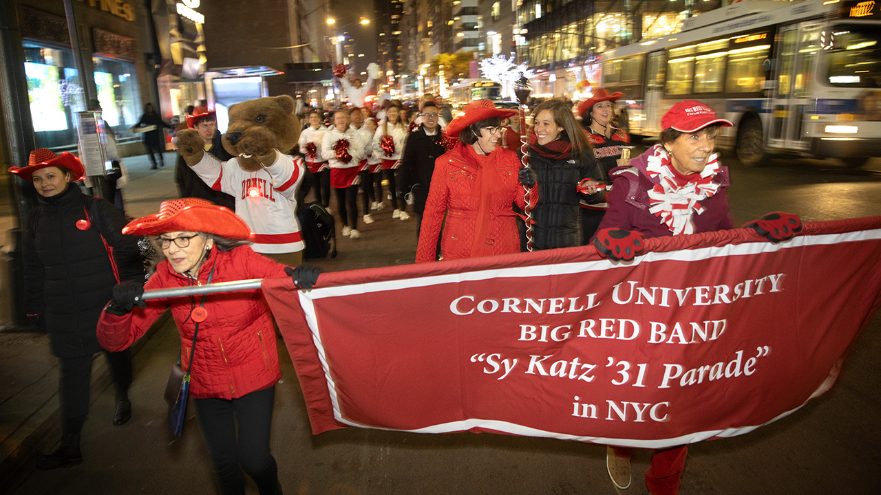 Two women hold a banner, followed by parade members in NYC at night.