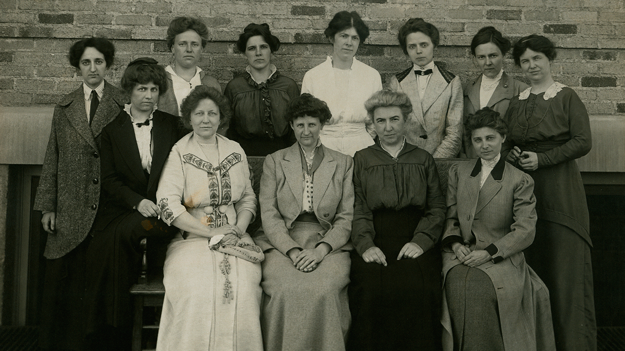 12 women posing for a group photograph, in Edwardian era clothing.