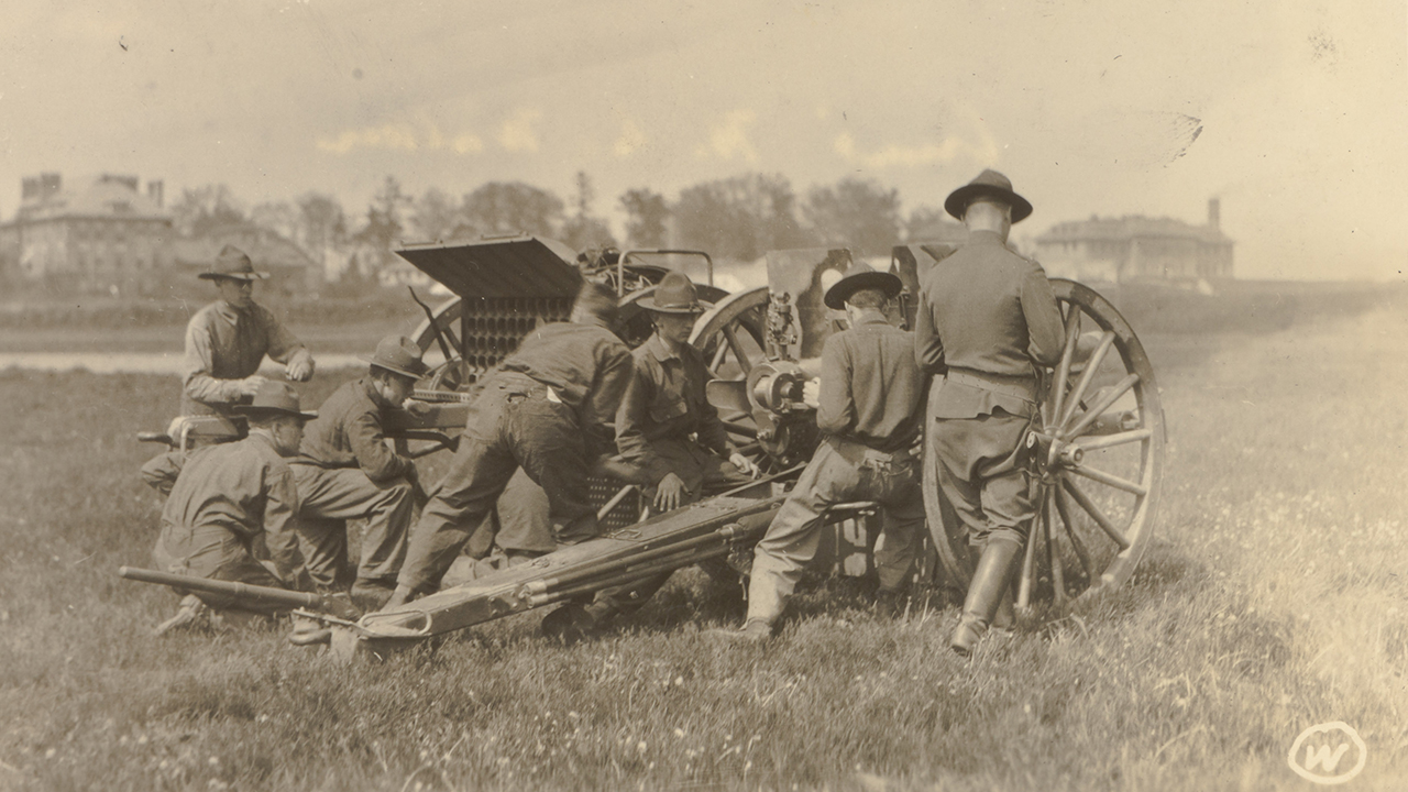 Seven men in uniform work around a large weapon on wheels in an open field.