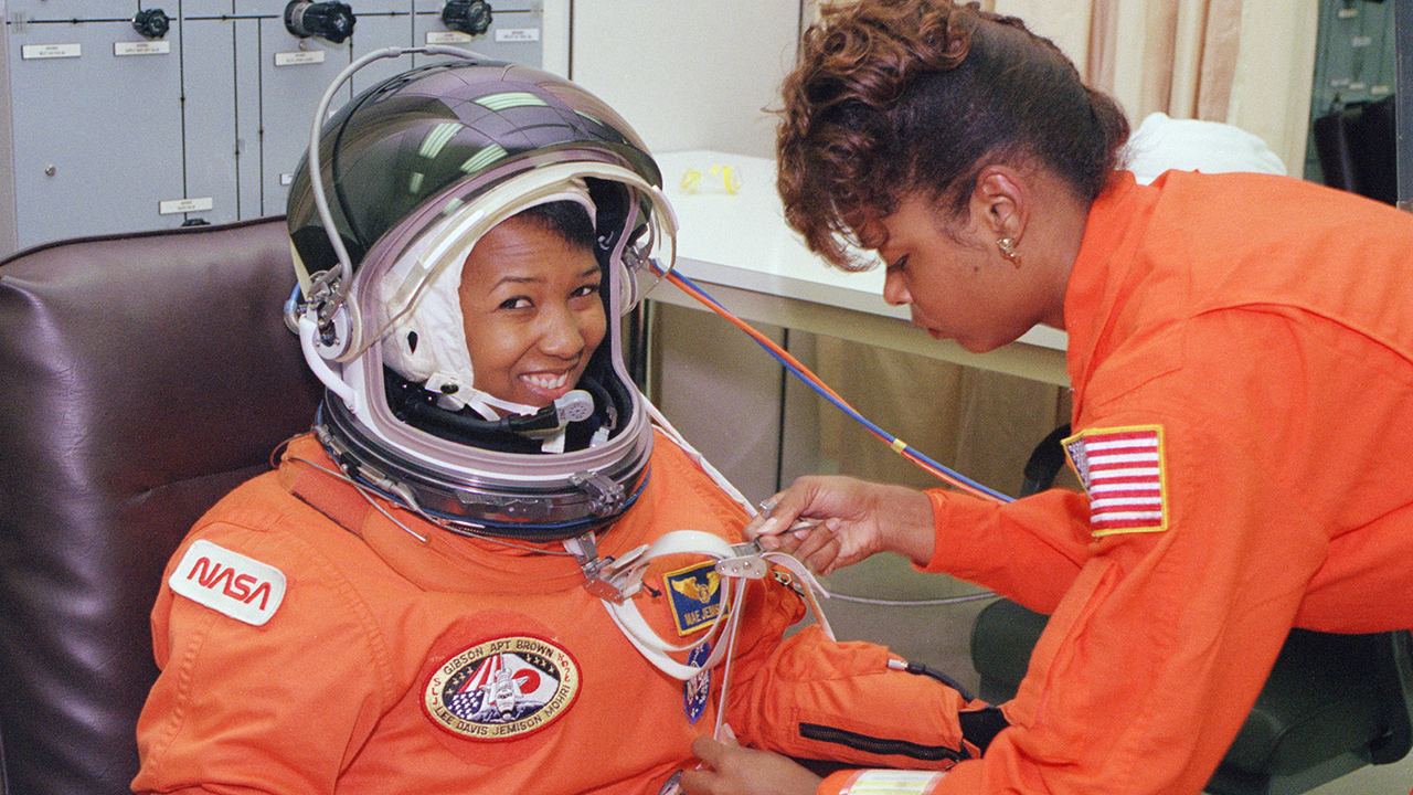 A smiling Mae Jemison is helped into her space suit by a NASA employee.