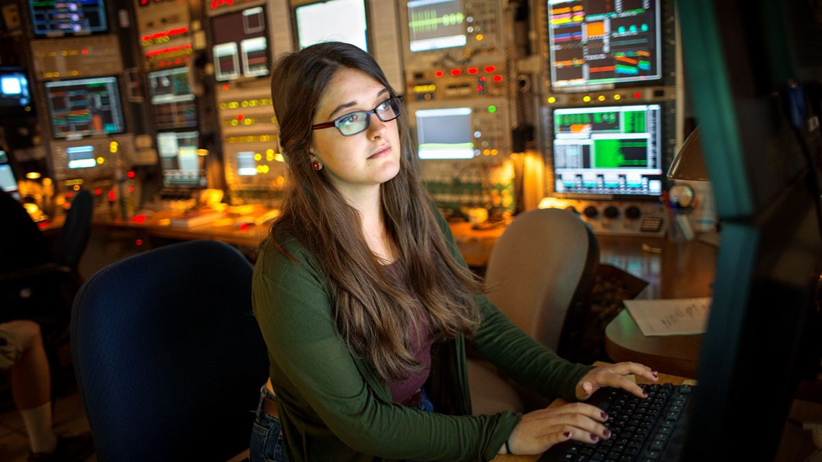 A young woman typing on a computer in a control room