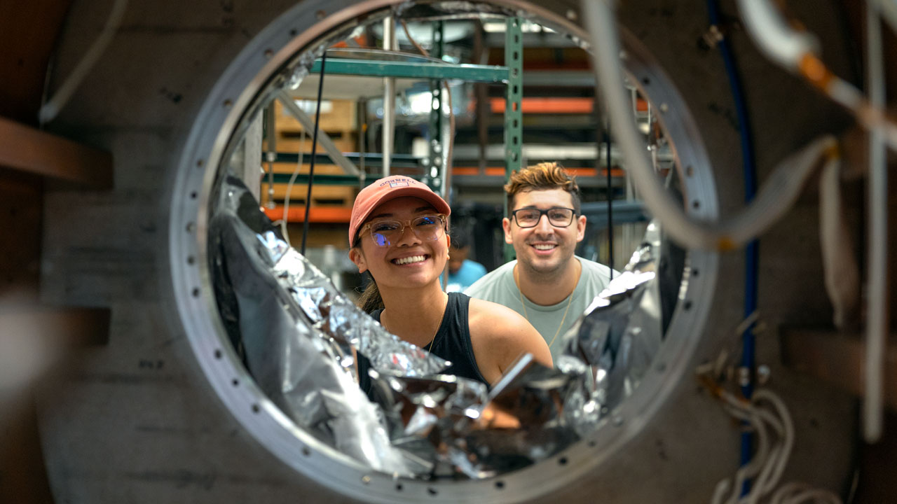 A female and male student peer through a metal tube.