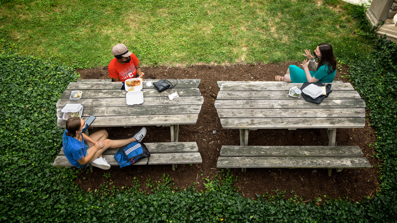 Students eat lunch at picnic tables outside
