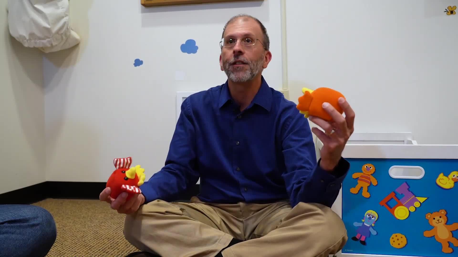 Michael Goldstein sits cross-legged on the floor holding baby toys